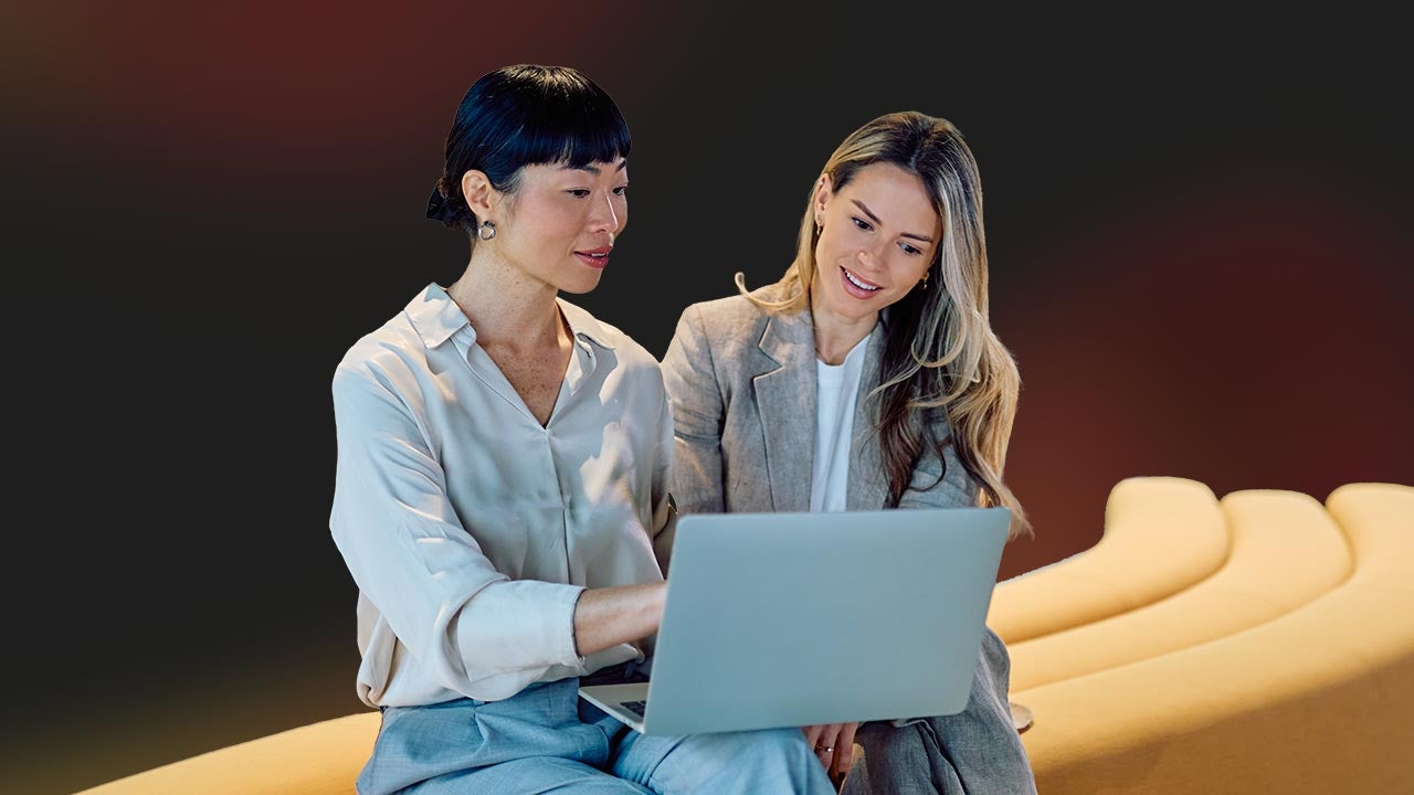 Two woman on a laptop in front of an abstract background