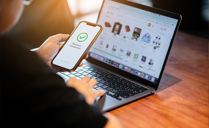 Mand, der handler på laptop og bruger sin telefon.