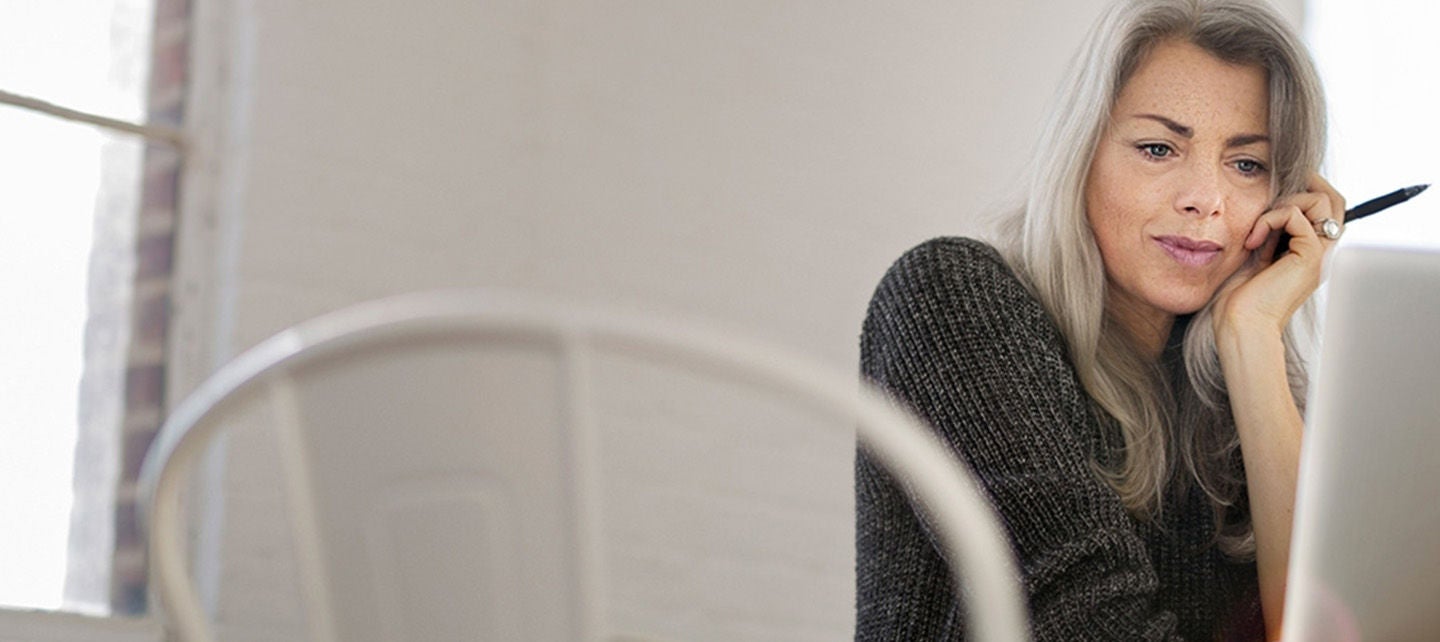 En person som sitter ved et bord, ser på en bærbar datamaskin og holder en penn mot ansiktet.