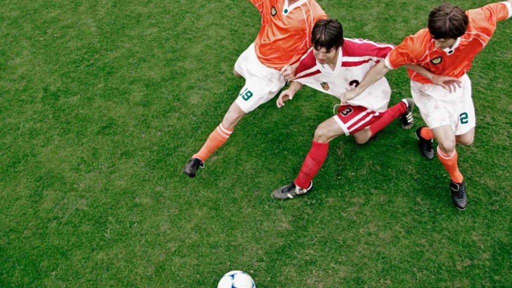 Three soccer players chase a soccer ball on a green field. 