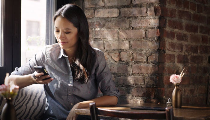 A young woman sits at a table in a coffee shop and checks her phone