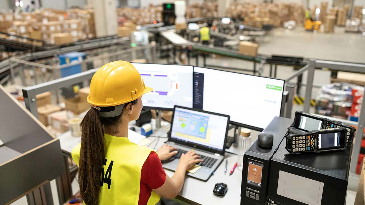 Woman using computer in large shipping warehouse.