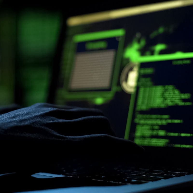 A person's hands hover over a keyboard on a laptop with coding on the screen in a darkened room. 