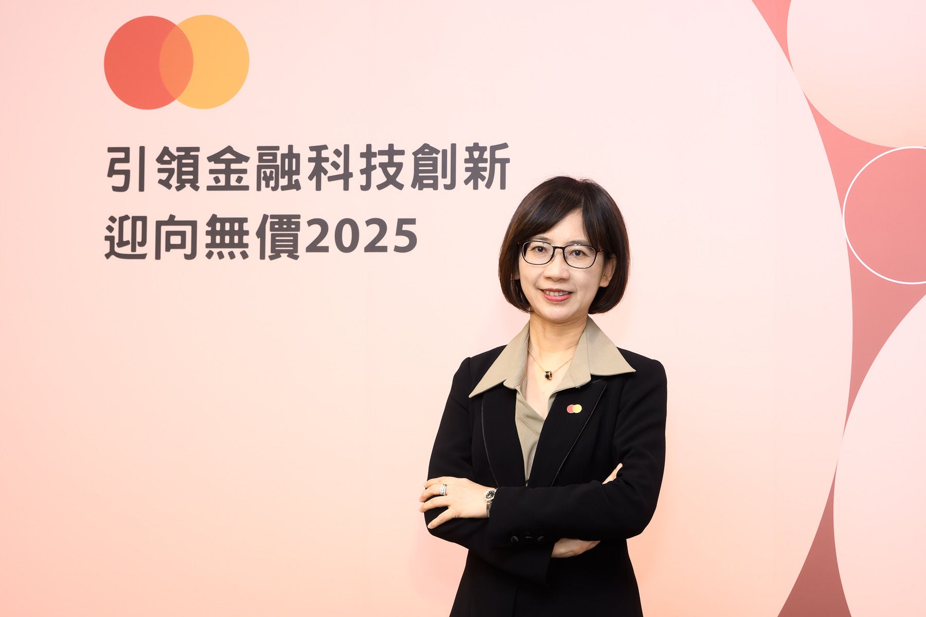 A woman in a black blazer stands with her arms crossed, smiling in front of a pale pink backdrop with Chinese text and a brand logo.