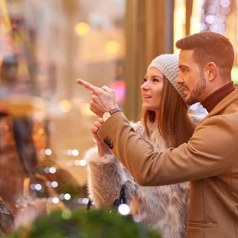 A woman with her hand around a man together look at a window display. 