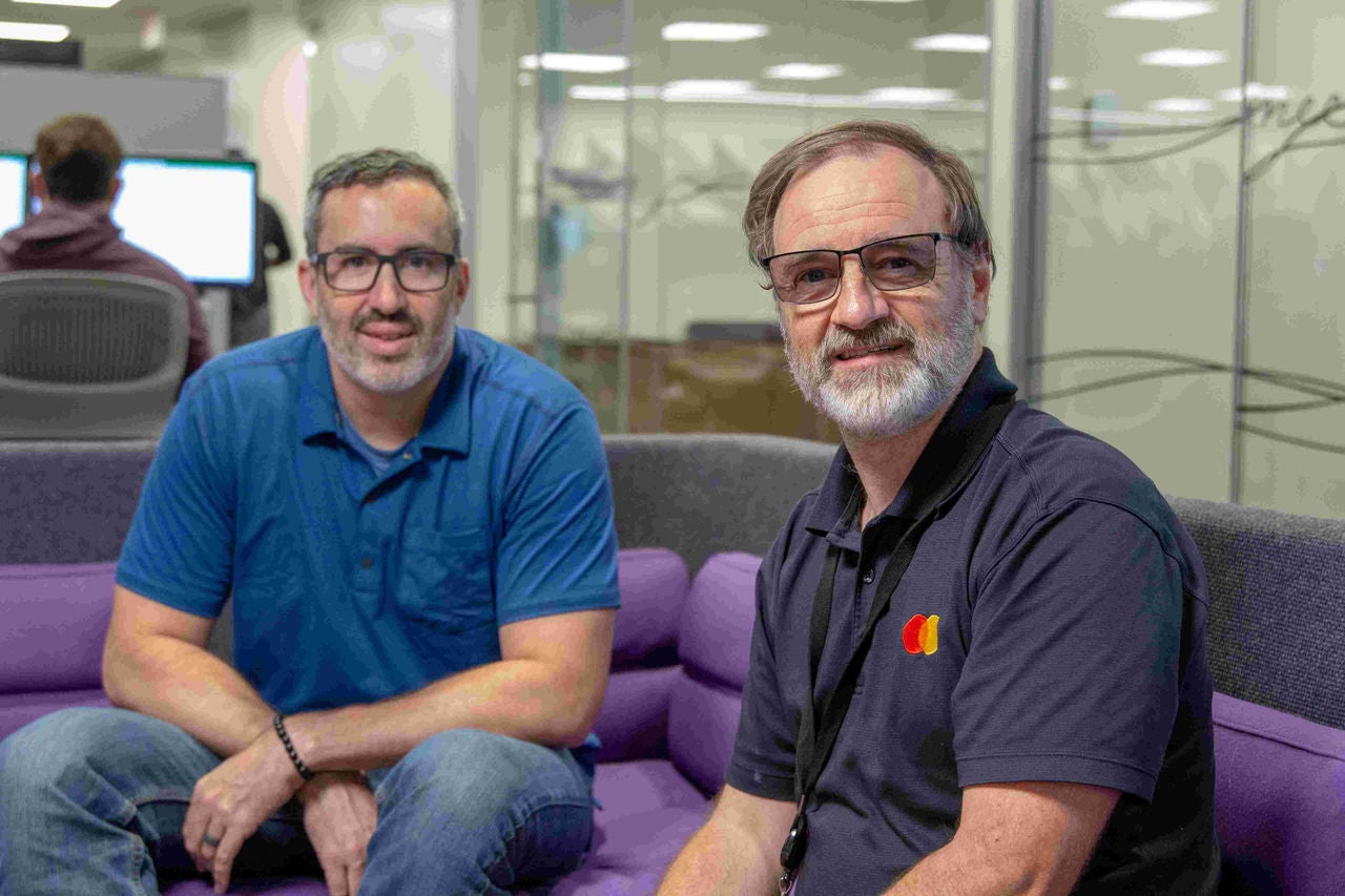 Brett Thomson and Vince Haulotte sit on a sofa in Mastercard's St. Louis Tech Hub. 