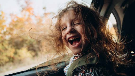 A child smiling with windblown hair and open car window.