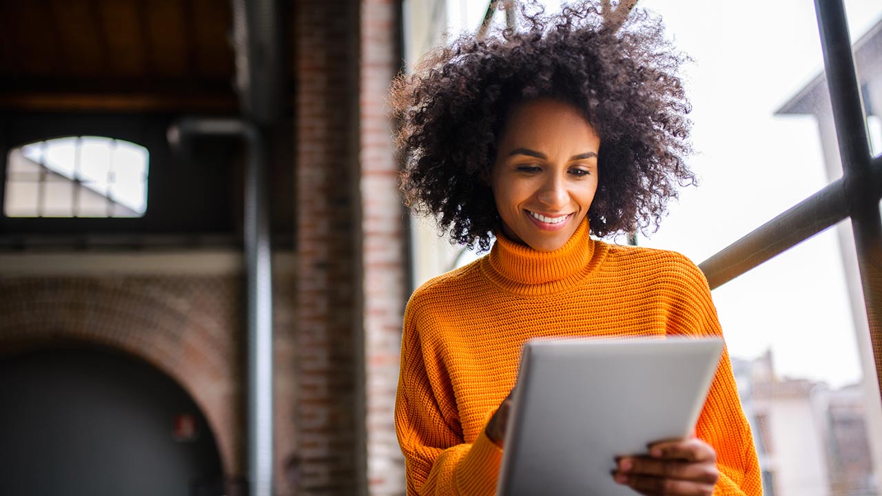 Smiling woman on tablet orange sweater.