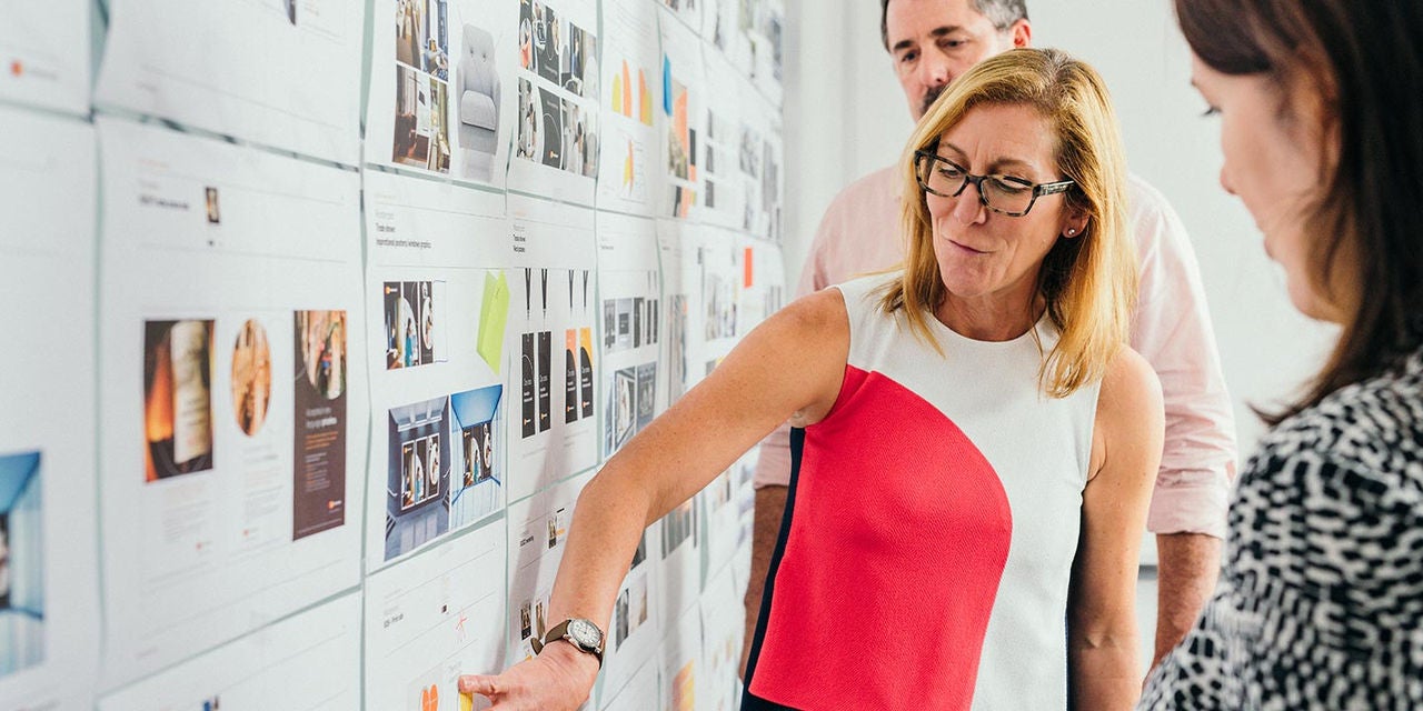Woman presenting ideas on a wall of design mockups while a colleague stands behind her.