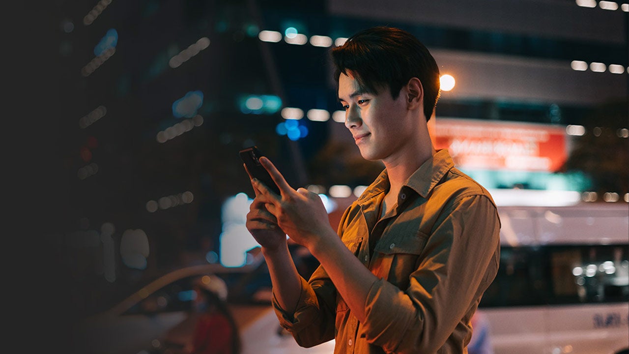 Man is using his phone while walking on the street at night.