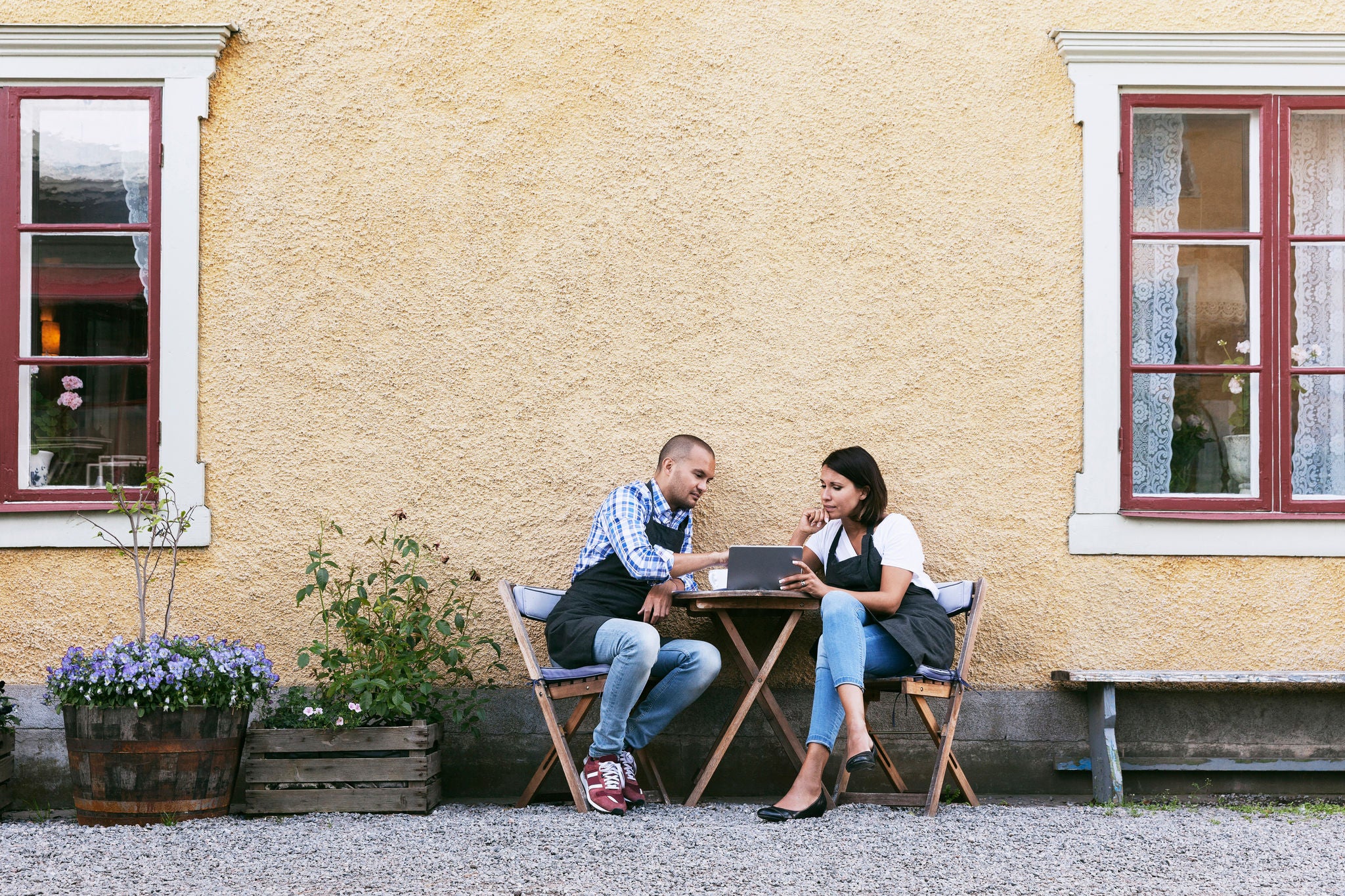 Bakers using digital tablet while sitting at table outside cafe