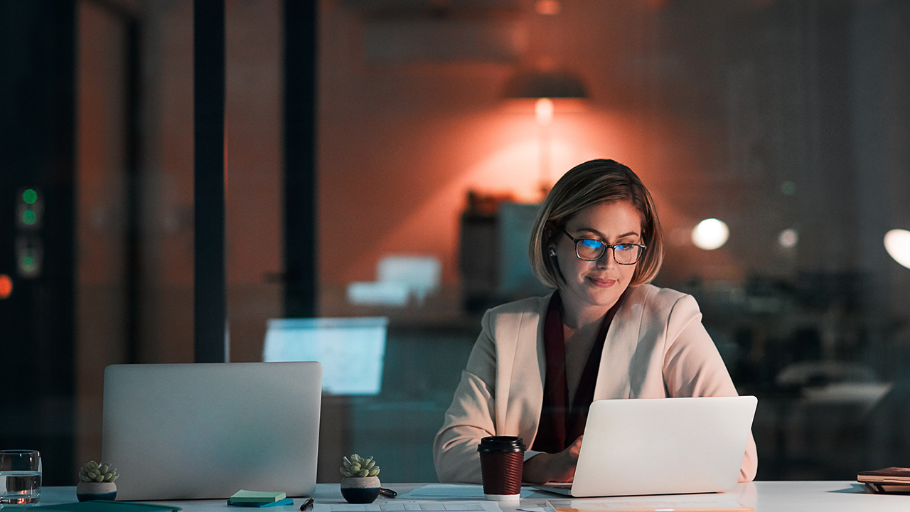 Woman with glasses working on a laptop at night.