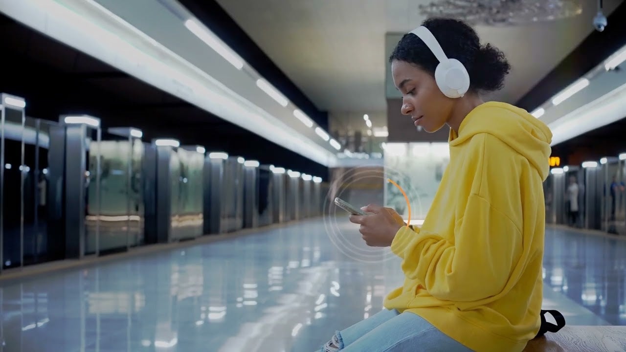 Woman wearing headphones sits while looking at her phone. 