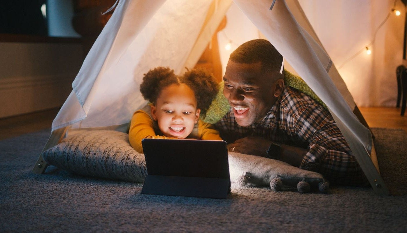 Father and his daughter in a tent in a the house looking at a laptop