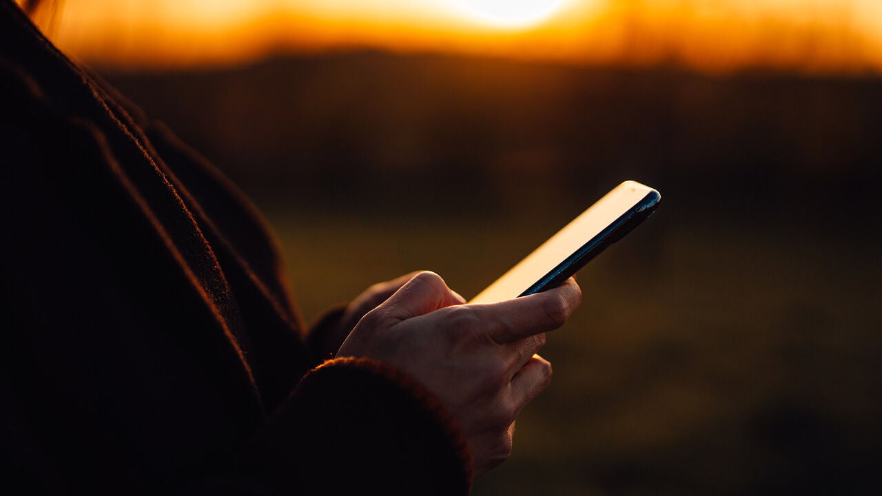 A person is holding a phone outdoors during sunset.