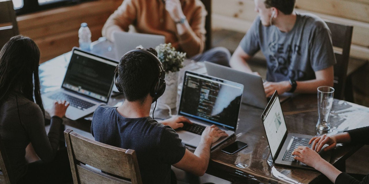 5 Personen arbeiten an ihren Computern an einem Tisch