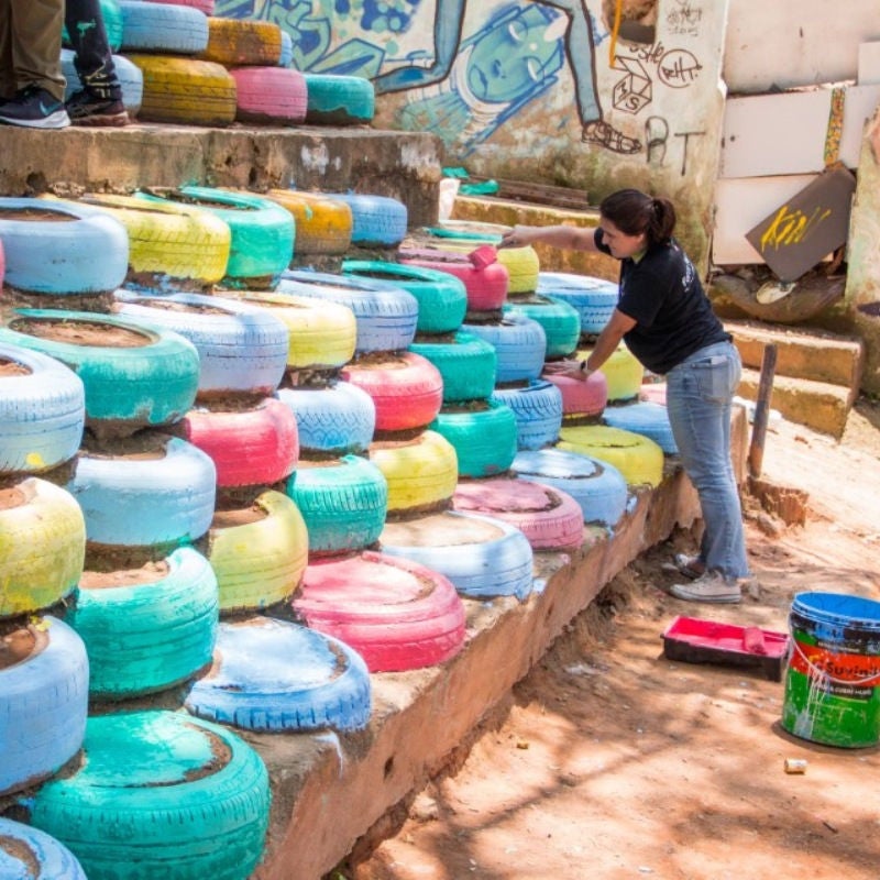 Rita Krejici paints tires stacked as a retaining wall . 