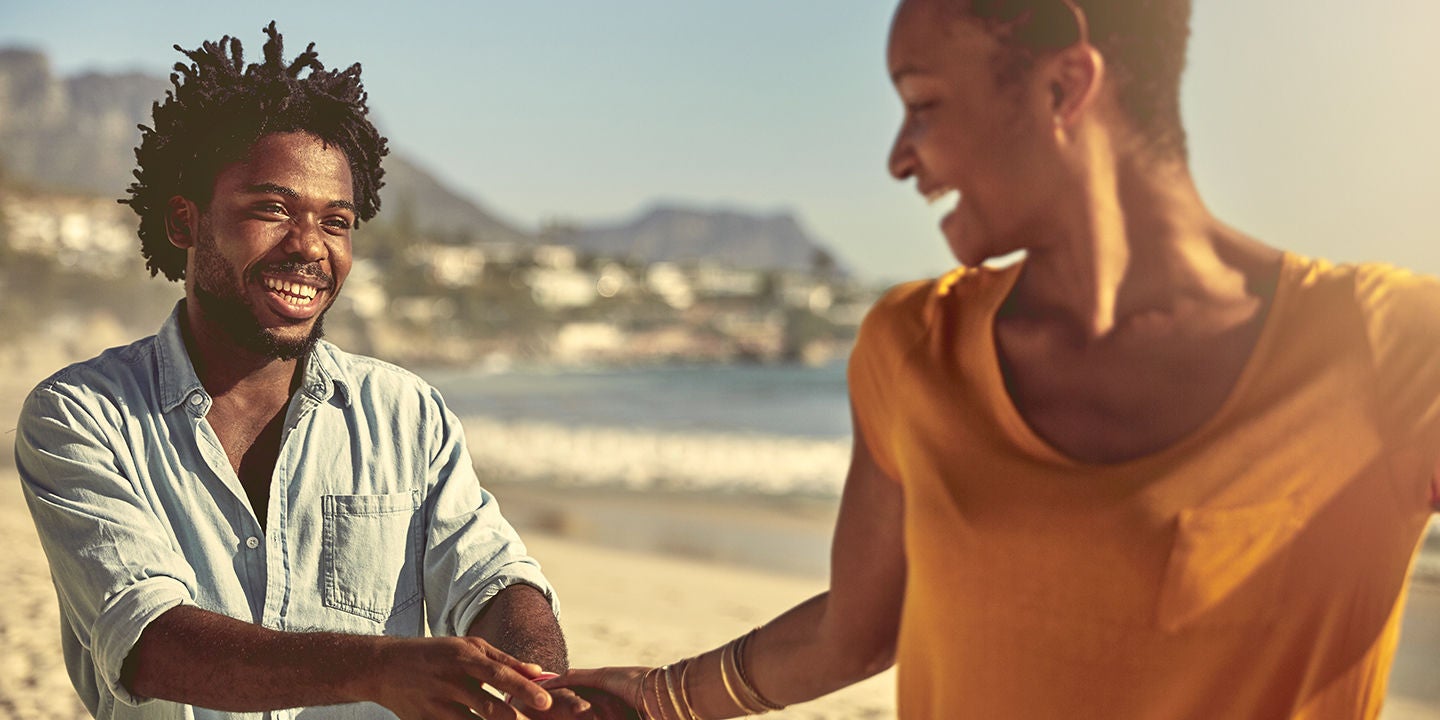 Playful young African American couple holding hands on sunny summer beach