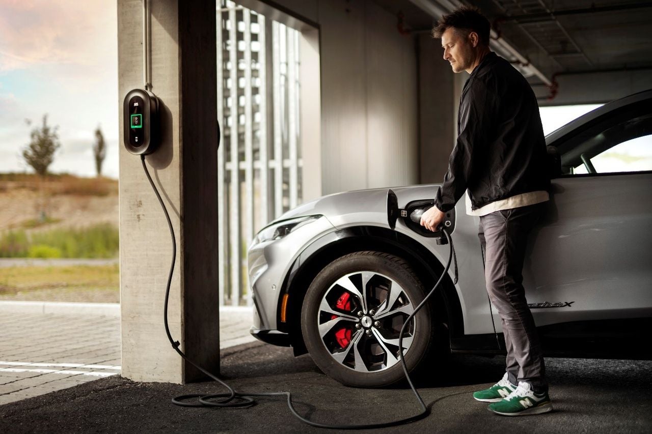 Person lader elbil inne i en garasje.