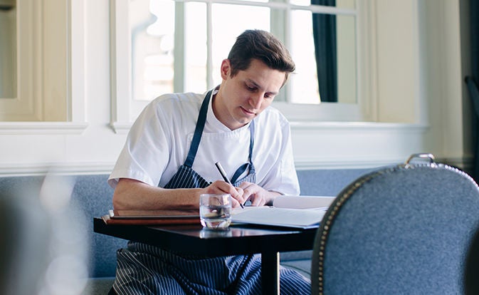 Chef writing notes at a restaurant table.