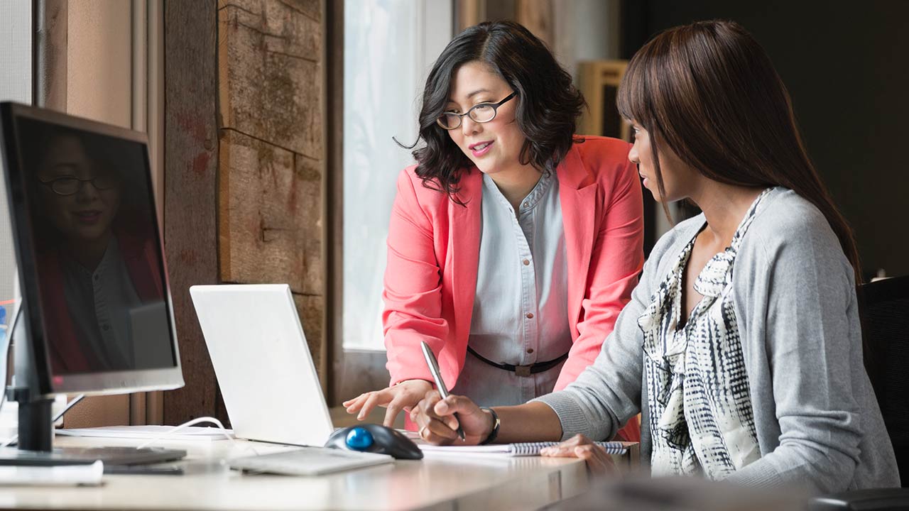 Female colleagues working on laptop at desk.