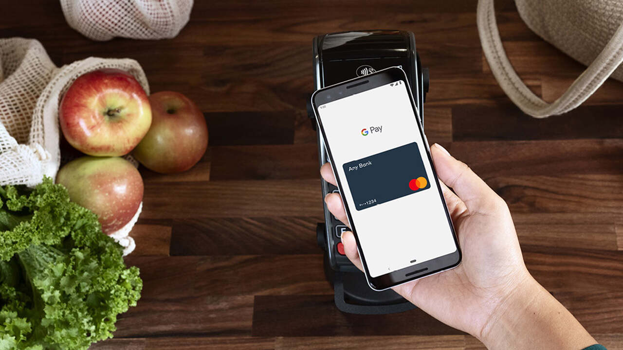 Okostelefonos érintéses fizetés Google Pay alkalmazással bankkártya-terminálnál, bevásárlás közben, gyümölcsökkel és vászontáskával az asztalon.