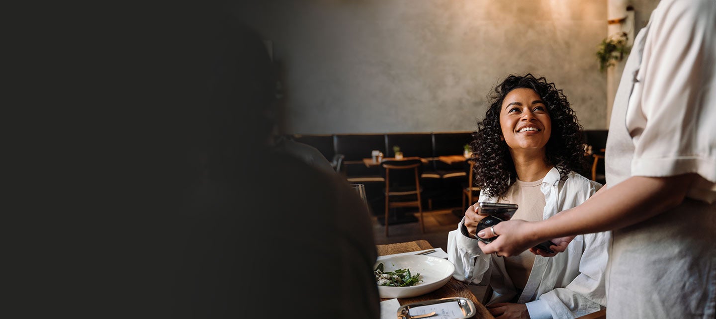 Woman paying a server on her phone at the table.