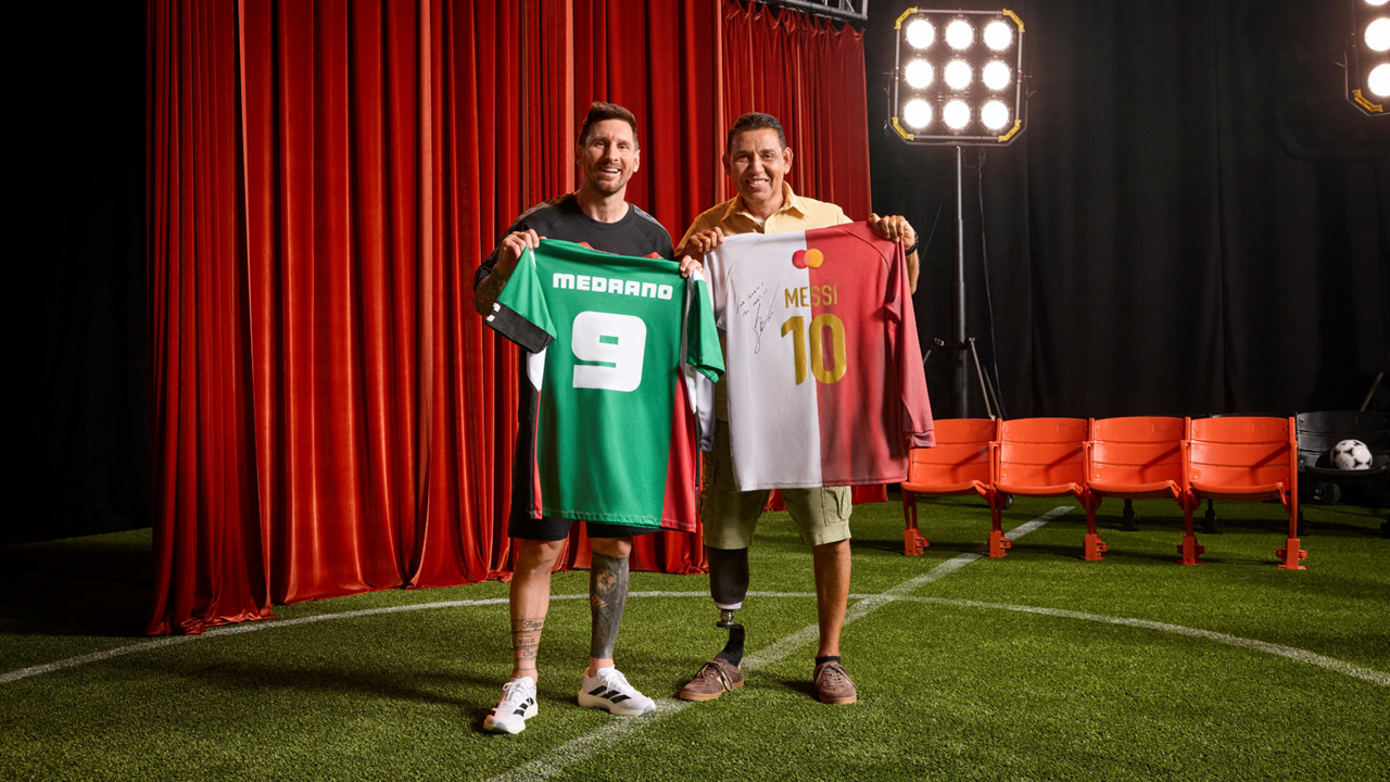 Lionel Messi smiling as he presents a signed black Messi #10 soccer jersey with a MasterCard logo to a male fan with dreadlocks during a promotional jersey exchange event.