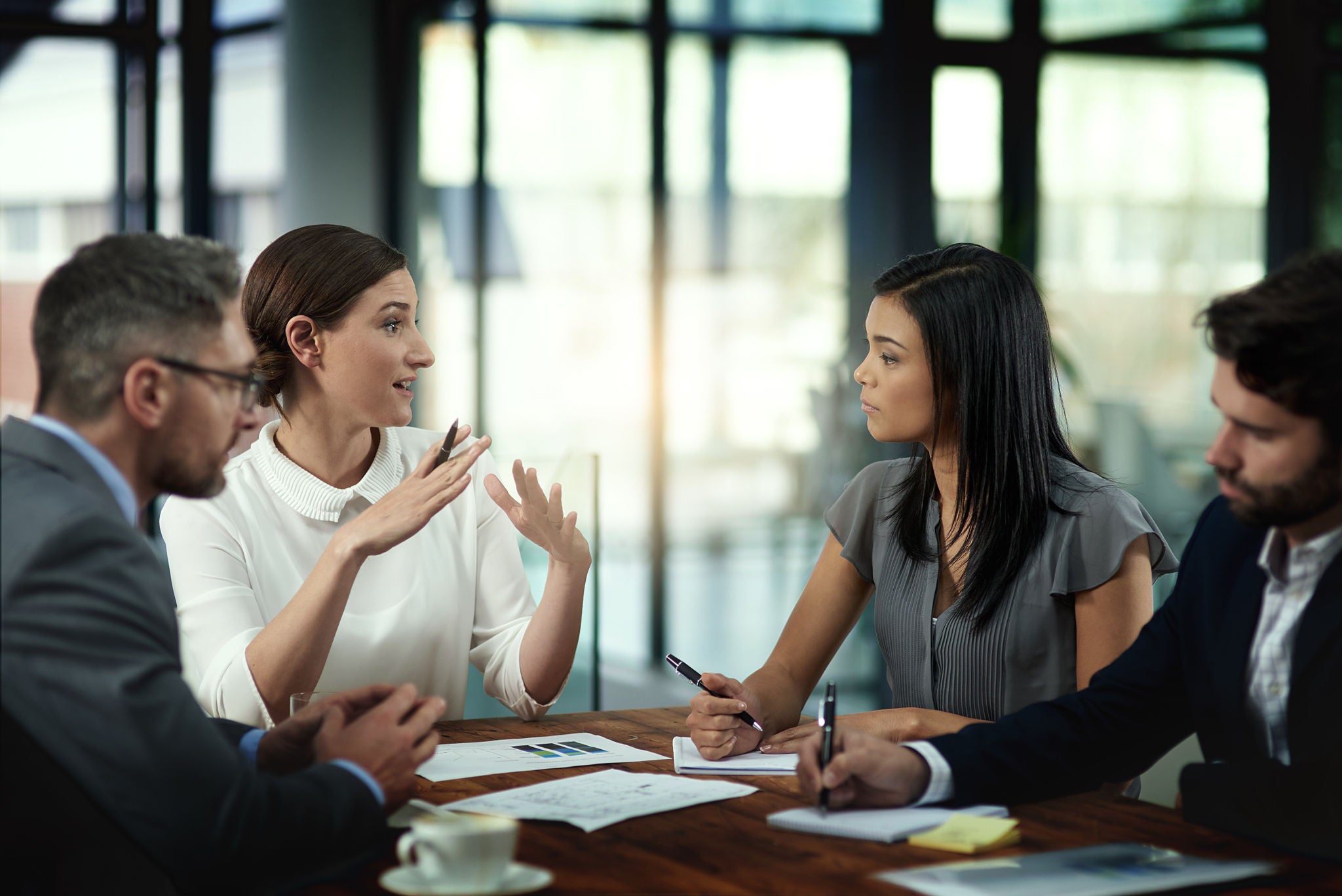 Group of women and men in a professional setting chatting around a conference table.