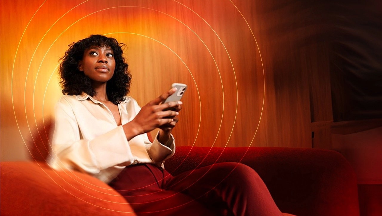 A woman sits on a chair and holds her phone while looking off to the side. 