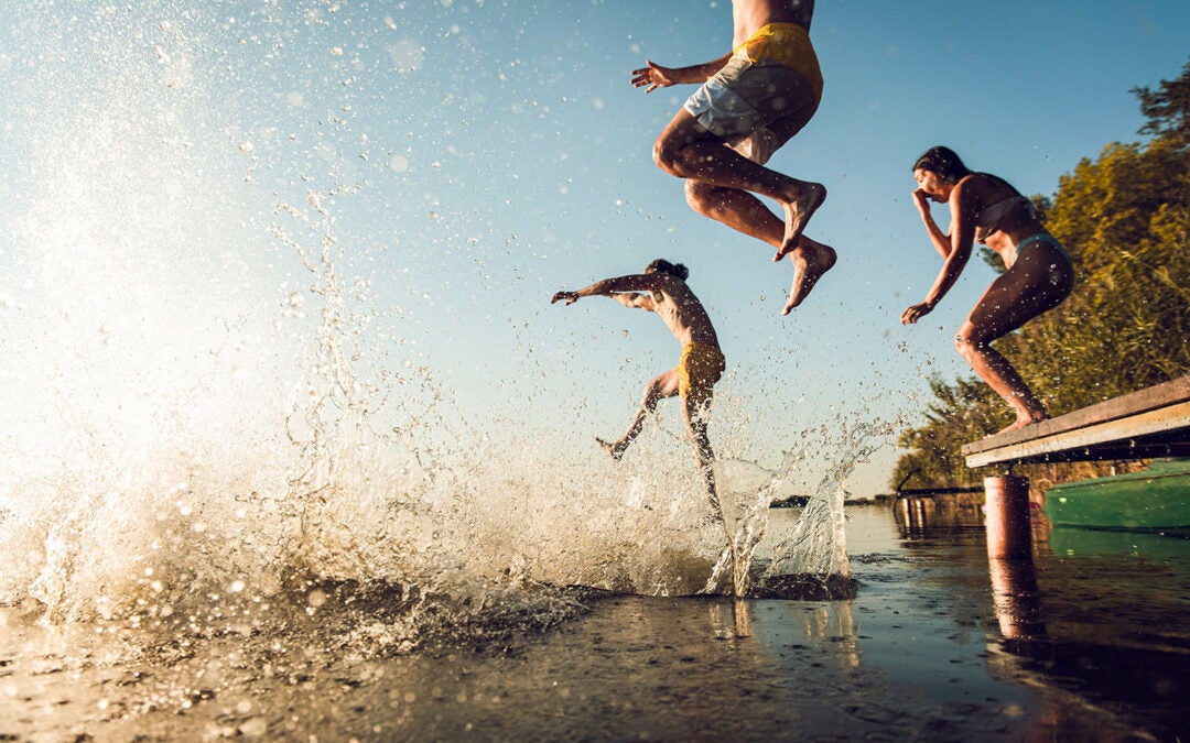 A group of friends jumping off a pier into a lake on a sunny day, representing how European consumers beat the summer heat.