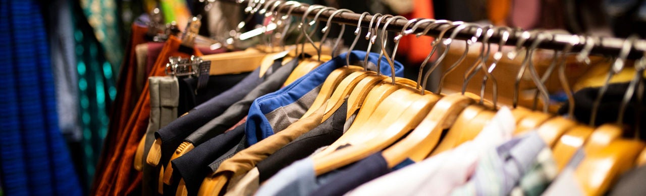 Ruhák fa vállfákon egy üzletben, különböző színekben és anyagokban, a tudatos és lassú divat hangulatát idézve.
