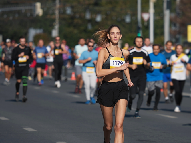 A young woman running  during a marathon with other participants in the background.