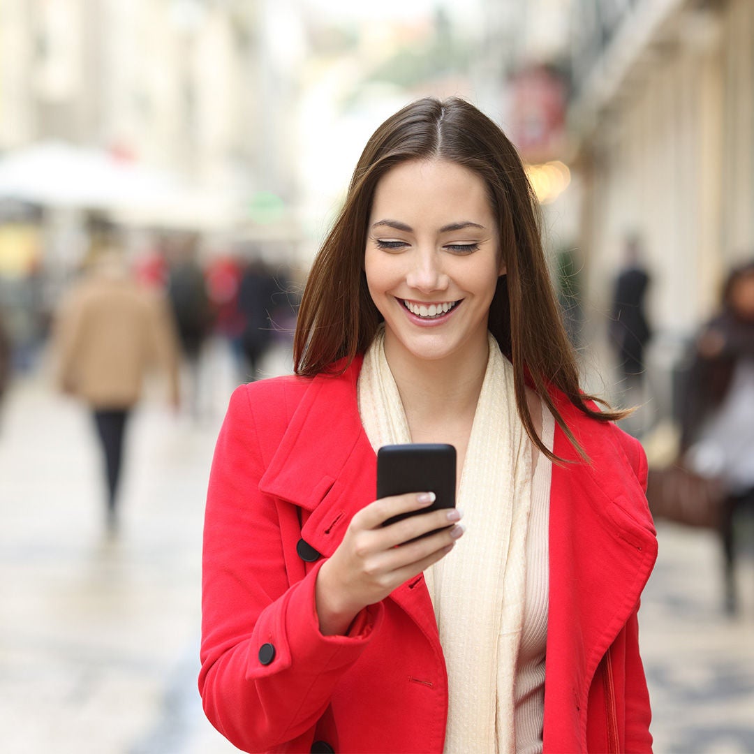 Girl in red over coat looking into mobile on street.