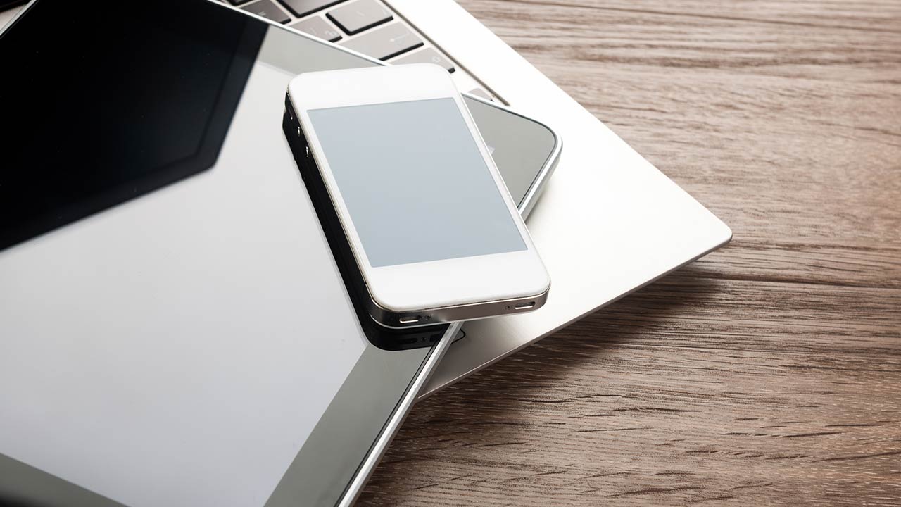 Keyboard with a phone and a tablet on a wooden desk.