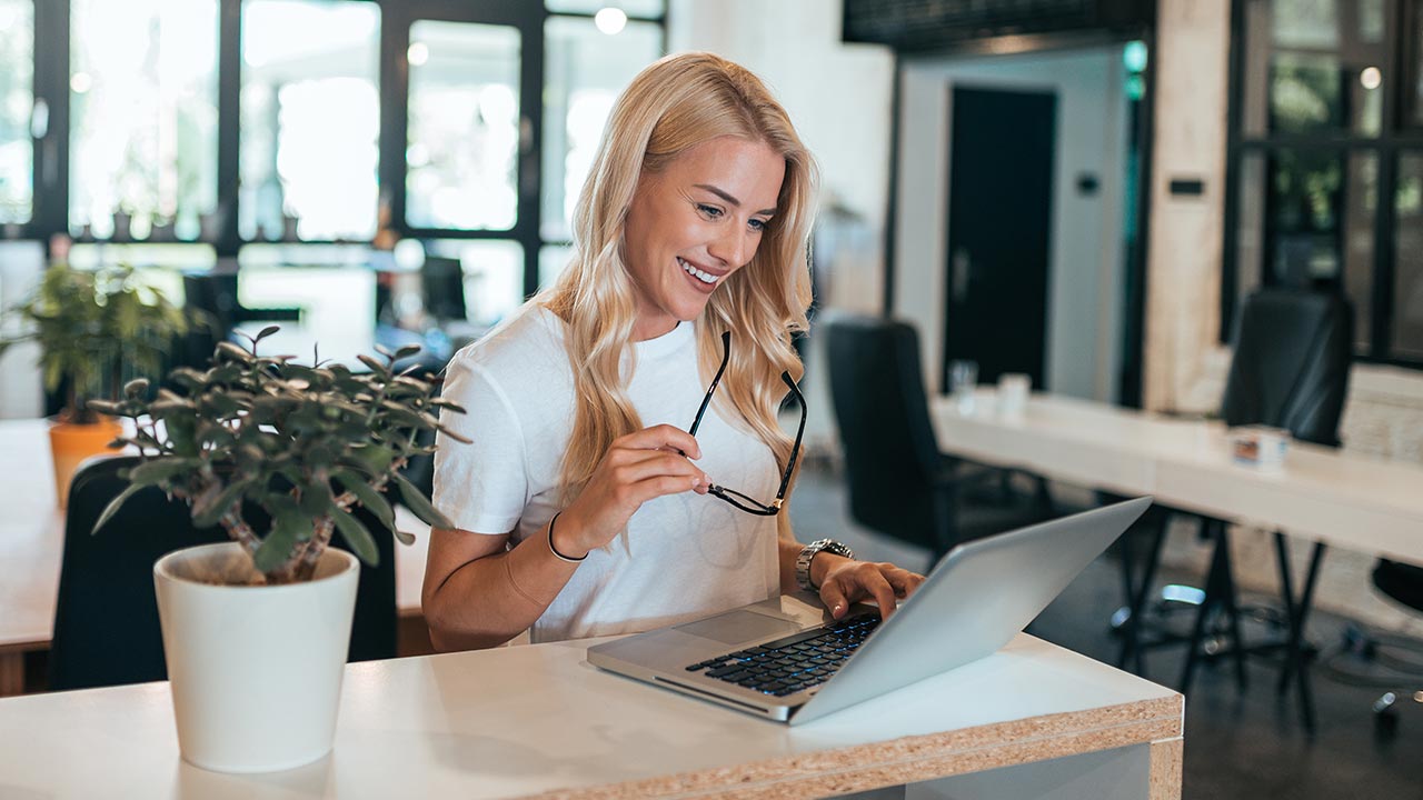 Happy woman focused on a laptop screen in an open office.