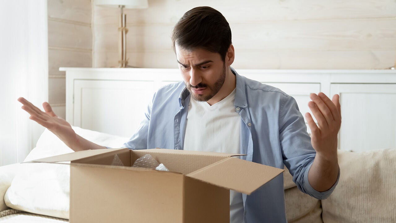 Meglepődött és csalódott férfi egy nyitott kartondobozt néz, amelyben hiányos vagy nem megfelelő rendelés érkezett.