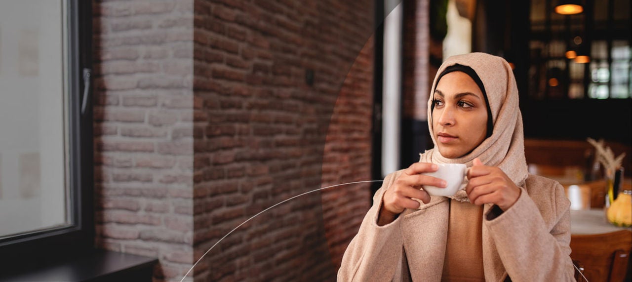 une femme portant un hijab tenant une tasse de café.