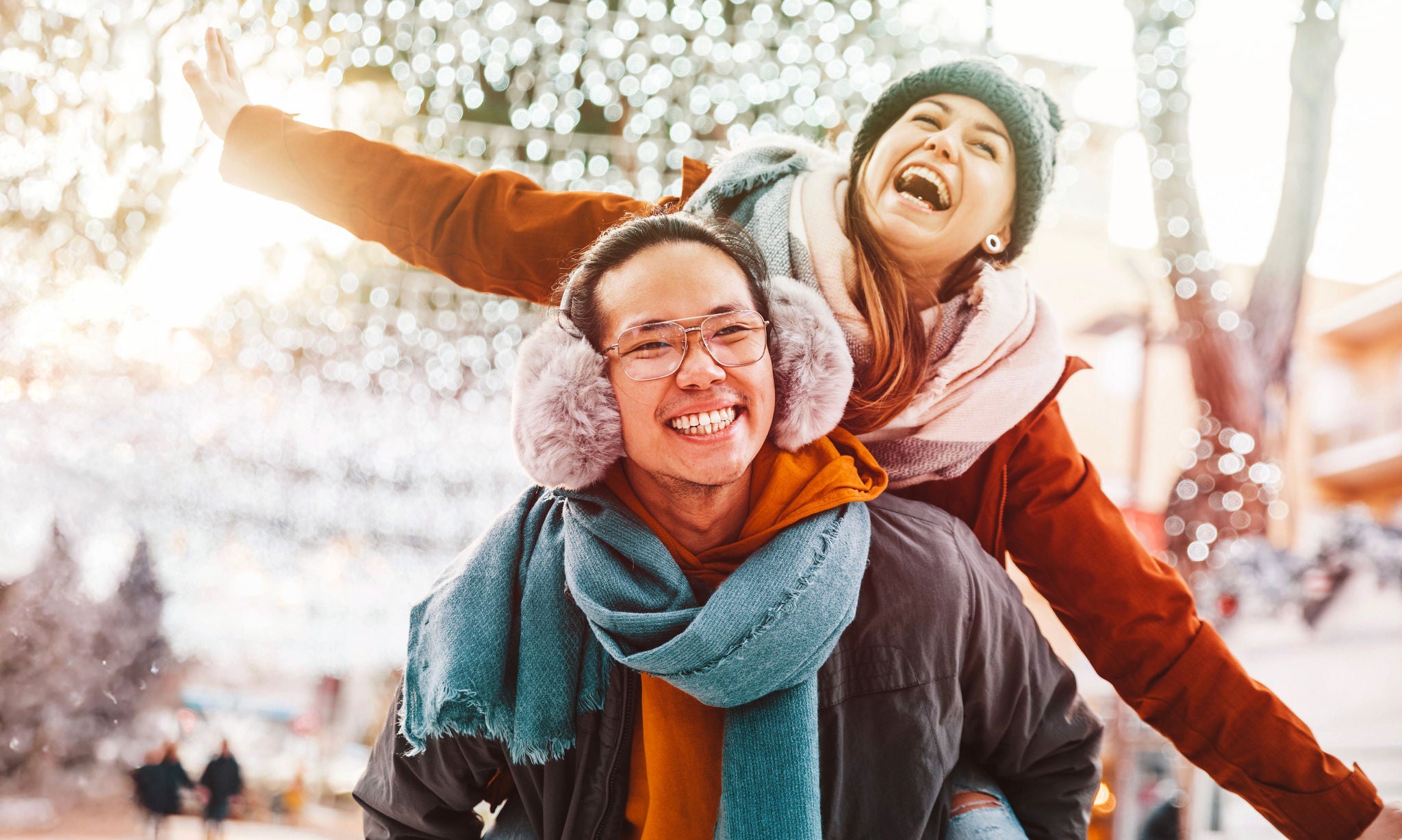 Multiracial couple in love wearing winter clothes celebrating Christmas holiday - Husband and wife having fun hanging out together walking on city street - Winter holidays and relationship concept