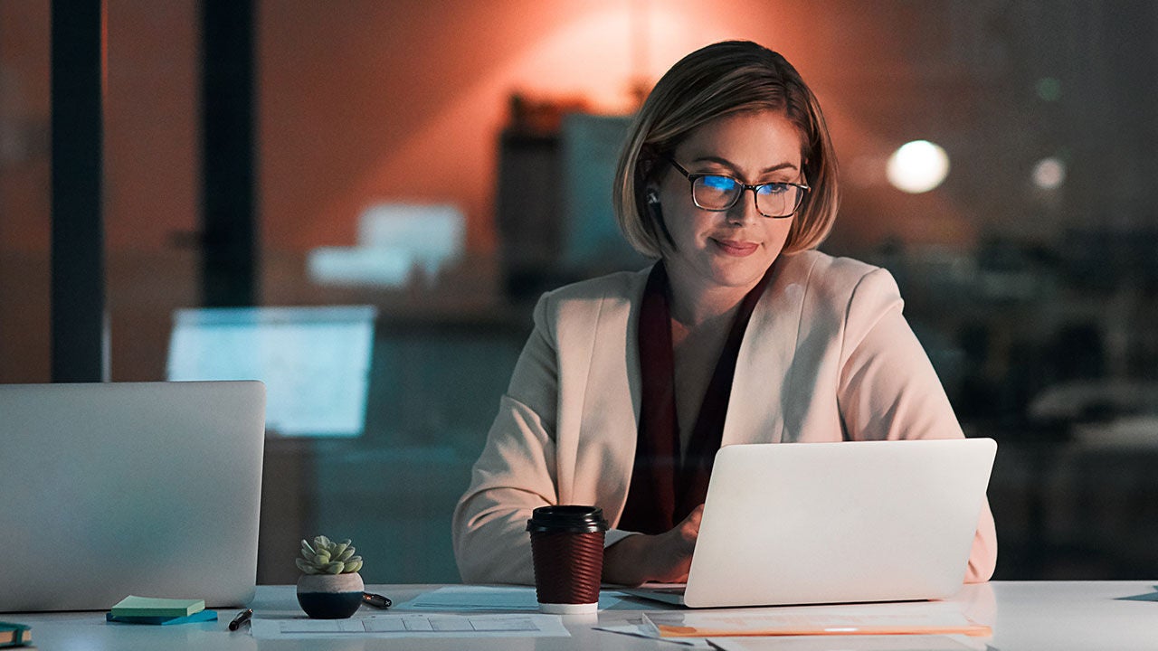 A businesswoman using a laptop at her desk during a late night at work.