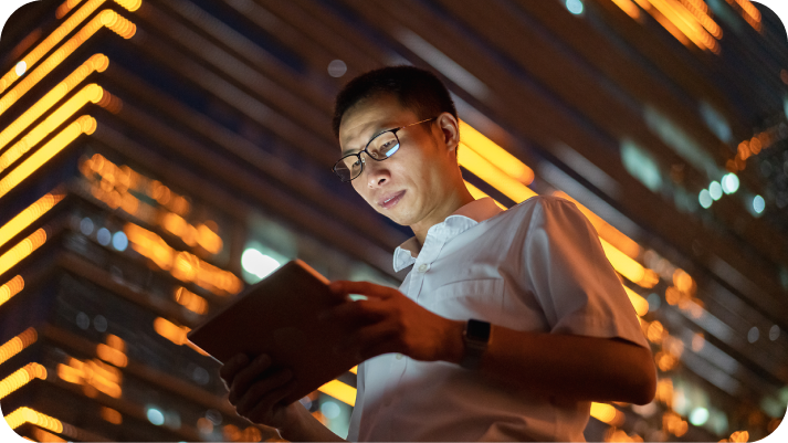 Man with tablet in front of building at night
