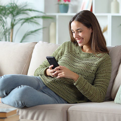 Woman using her smartphone while laying on the sofa