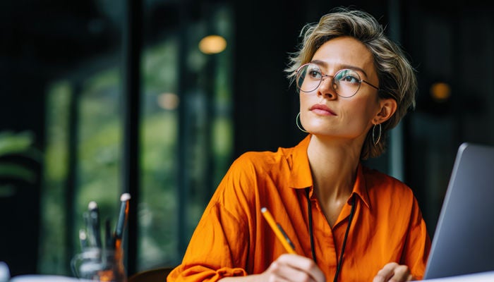 Woman on her laptop taking notes with a pencil
