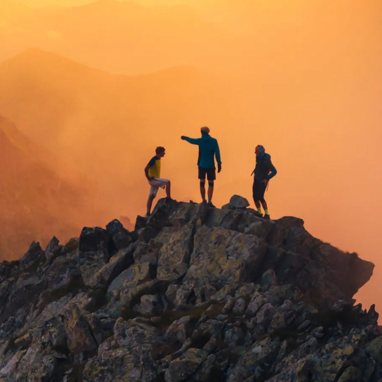 Three hikers standing on a rocky peak at sunset.