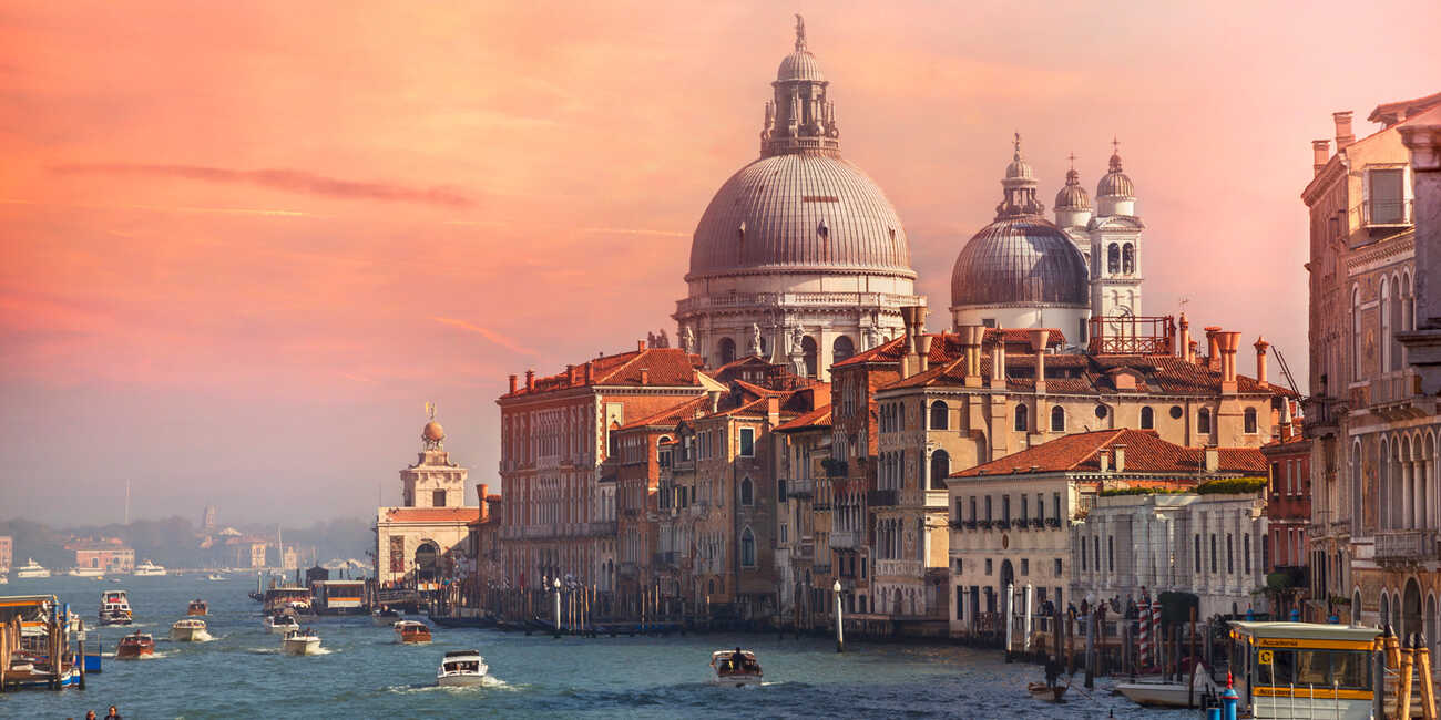 Velence Grand Canal látképe naplementében, a Santa Maria della Salute bazilikával és csatornán haladó hajókkal.
