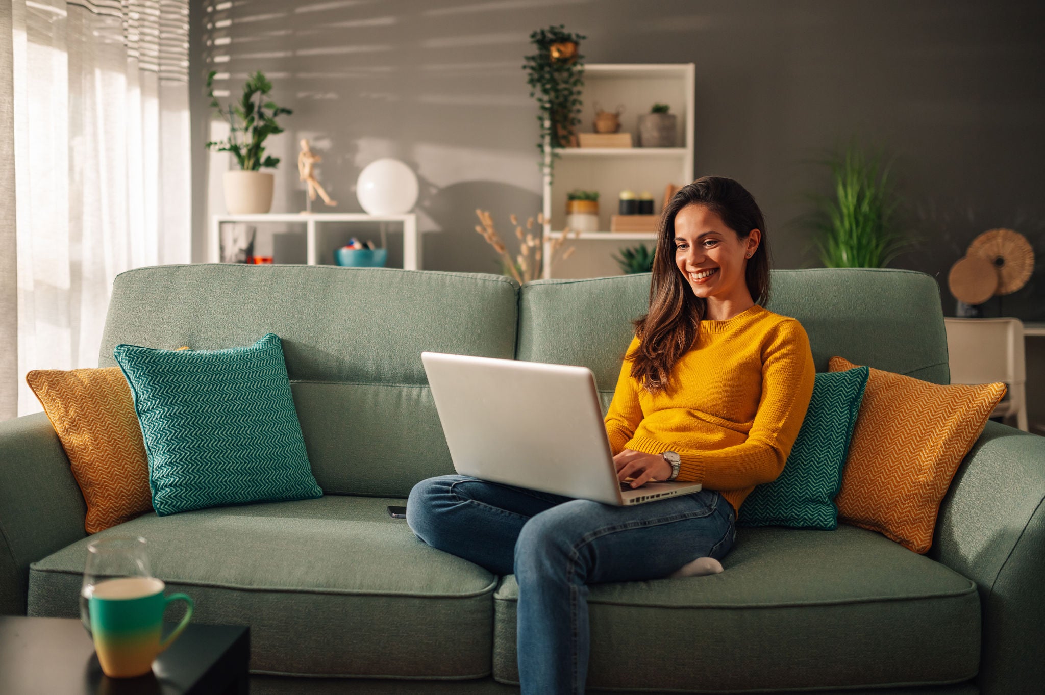 Woman smiling while using laptop while sitting on couch.