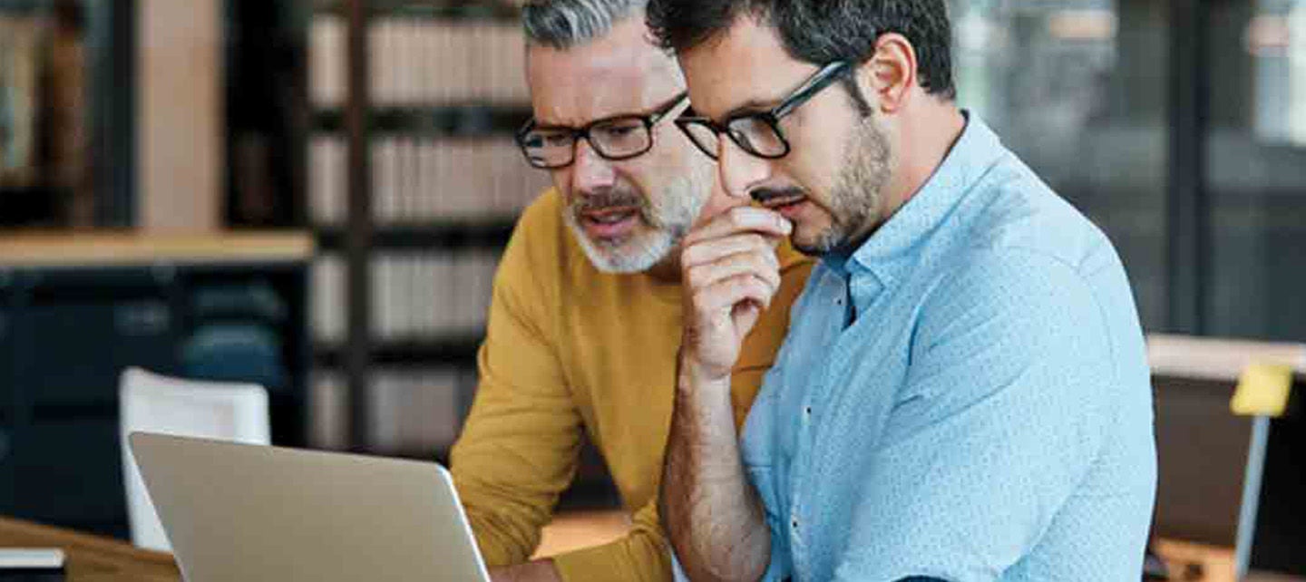 To menn diskuterer noe viktig mens de ser på laptop skjermen sammen.