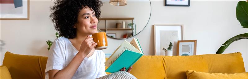 Woman sitting on a sofa with a cup of coffee reading a book