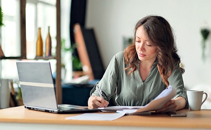 Woman writing on paper while using a laptop