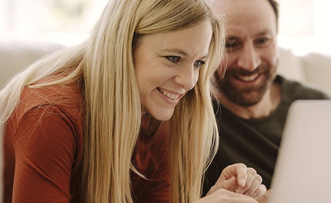 Woman smiling while looking at a laptop with a coworker nearby.